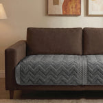 Brown sofa with a gray quilted cover in a living room setting.